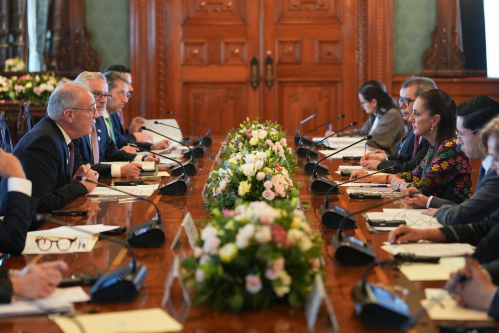 HMukfpKWwAEx2xx - Petróleo y Energía Formal meeting with officials seated along a long wooden conference table covered in documents and microphones, in a grand room with floral centerpieces.