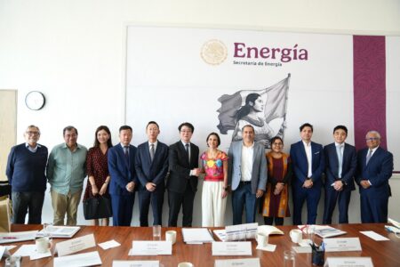 Group of professionals in formal attire posing for a photo in front of an Energie banner in a conference room, with a wooden table and documents in the foreground.