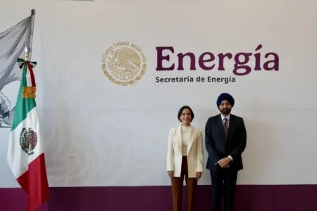 Two officials stand beside a wall with the word Energia and the Mexican government seal; Mexican flag on the left.