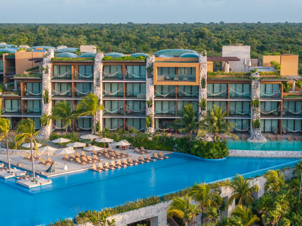 default - Petróleo y Energía Aerial view of a tropical resort with glass-front balconies, hammocks, palm trees, and a large blue pool.