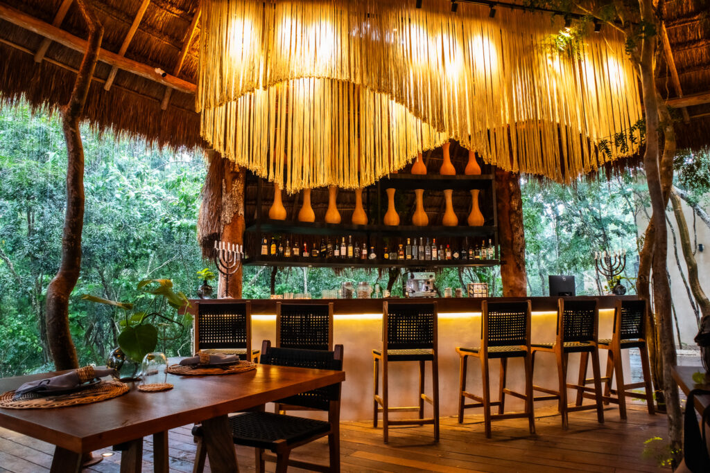 MESTIZO MISTERIO CULINARIO 1 jpg 1 - Petróleo y Energía Outdoor tropical bar under a thatched roof with long straw curtains and a liquor shelf behind the counter.
