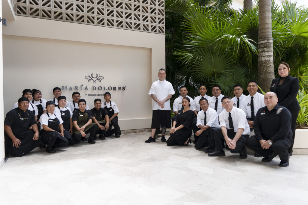 - Petróleo y Energía Group of restaurant staff in uniforms posing outdoors next to a sign that reads'MARÍA DOLORES' with tropical plants in the background