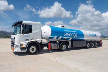 White truck with a blue HVO 100 diesel tanker parked on a tarmac at an airfield, mountains in the distance.