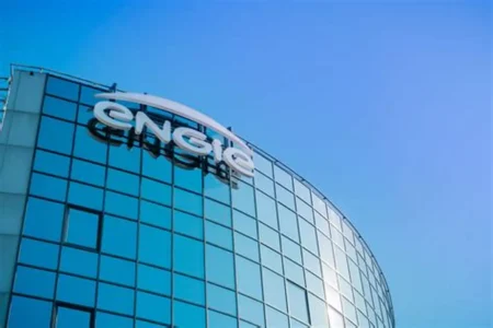 Curved glass office building with a white company logo on the rooftop against a blue sky.