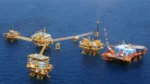 Offshore oil drilling complex with yellow platforms connected by a long walkway in a blue sea area.