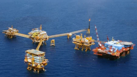 Offshore oil drilling complex with yellow platforms connected by a long walkway in a blue sea area.