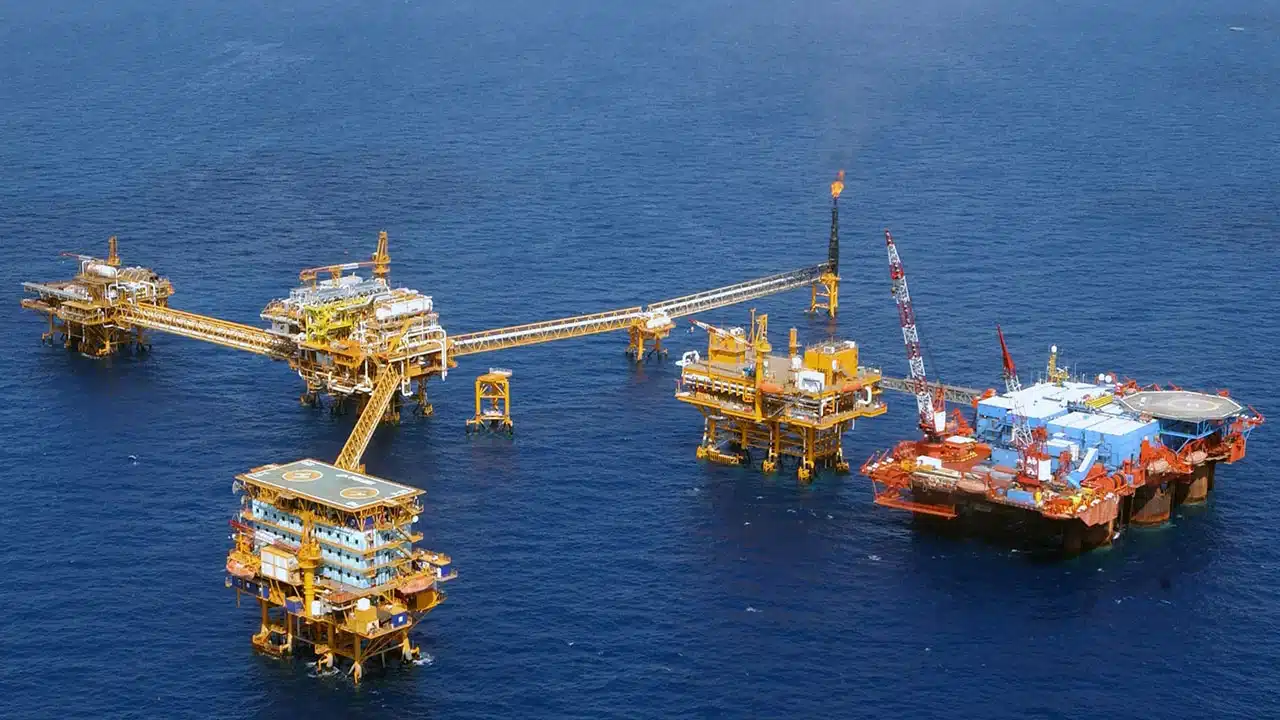 Offshore oil drilling complex with yellow platforms connected by a long walkway in a blue sea area.