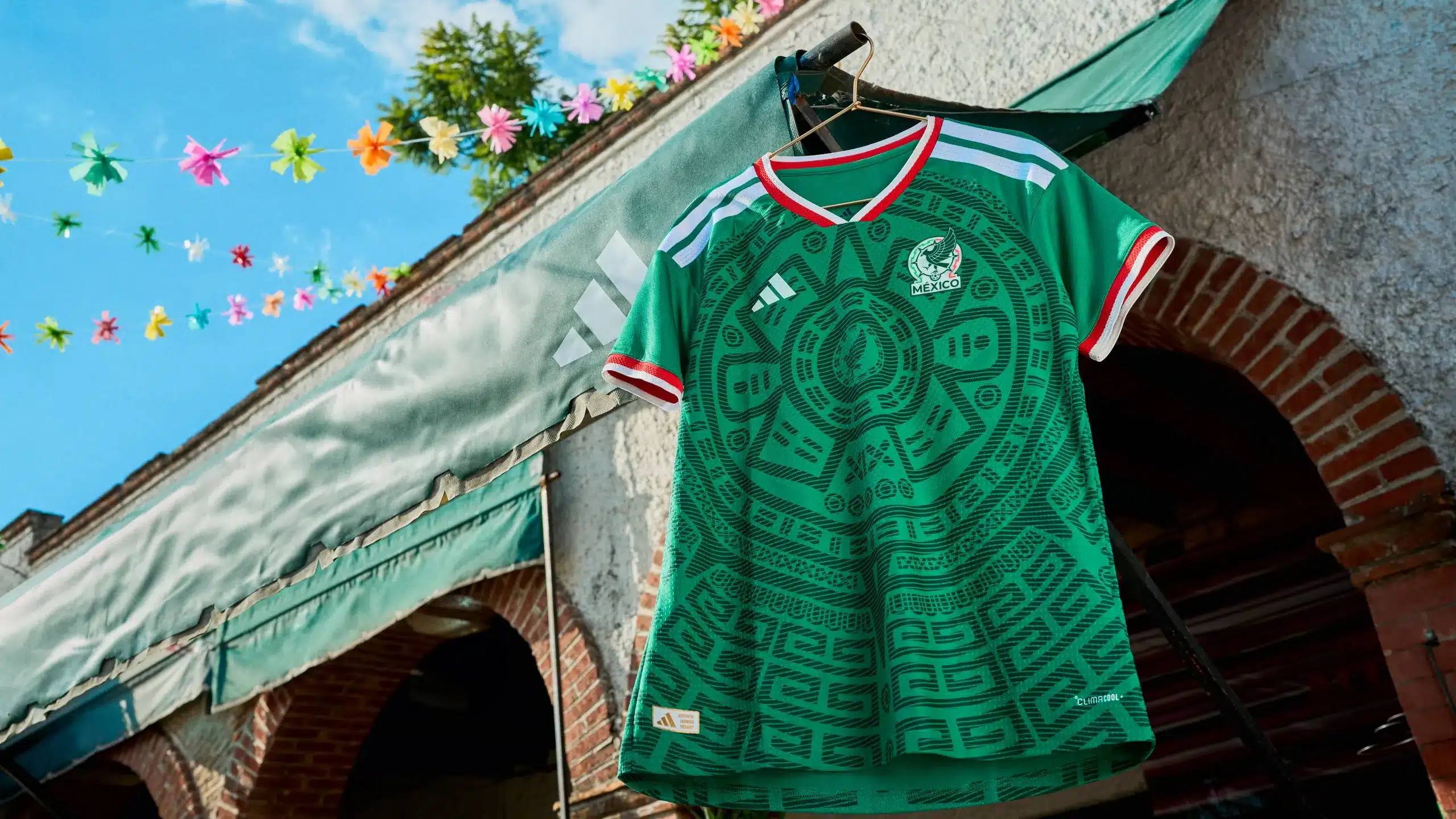 Green Mexico football jersey hanging on a clothesline outdoors with colorful garlands and a brick building nearby.