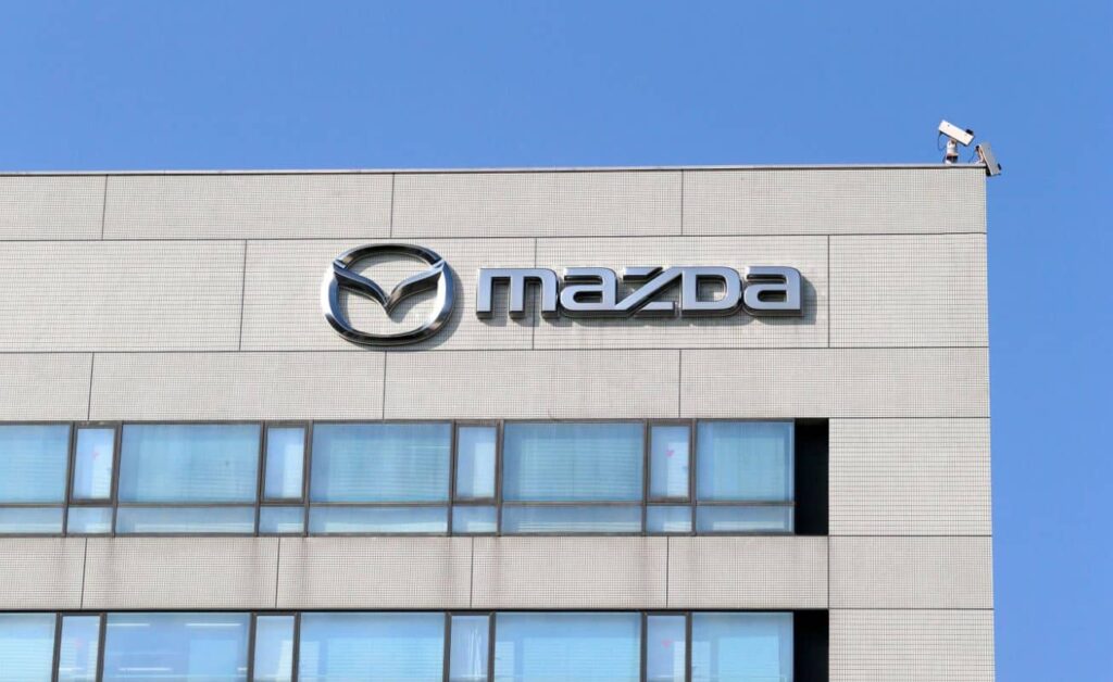 Mazda logo on the beige tiled exterior of a building against a blue sky.