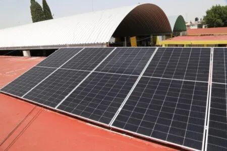Solar panels installed on a red roof with curved white and green structures in the background, likely part of a solar energy setup