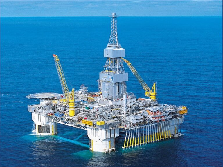 Offshore oil platform in the blue ocean with tall derrick and yellow cranes.