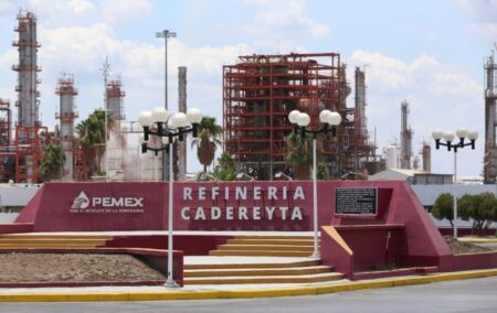 Entrance monument to Refinería Cadereyta, Pemex, with red steps and sign, industrial refinery towers in the background.