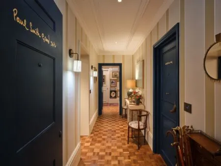 Narrow hallway in a stylish home with cream striped walls, dark blue doors, and a parquet floor, leading to a warmly lit room.