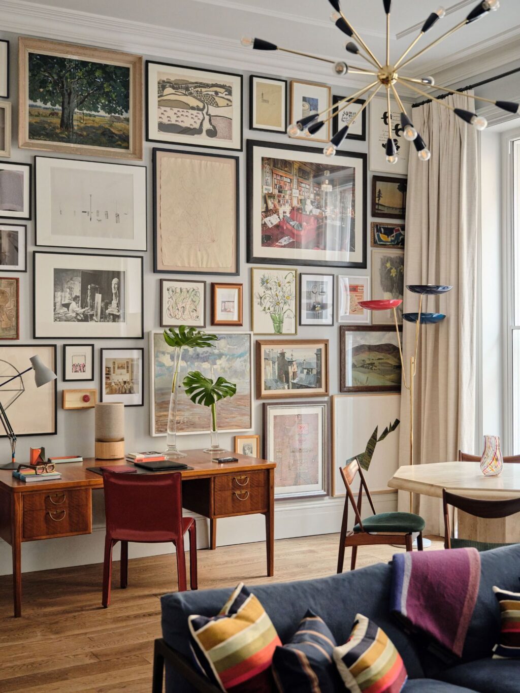 RFHBRO~1 - Petróleo y Energía Wall filled with framed artwork above a wooden desk and red chair in a bright, gallery-style living room.