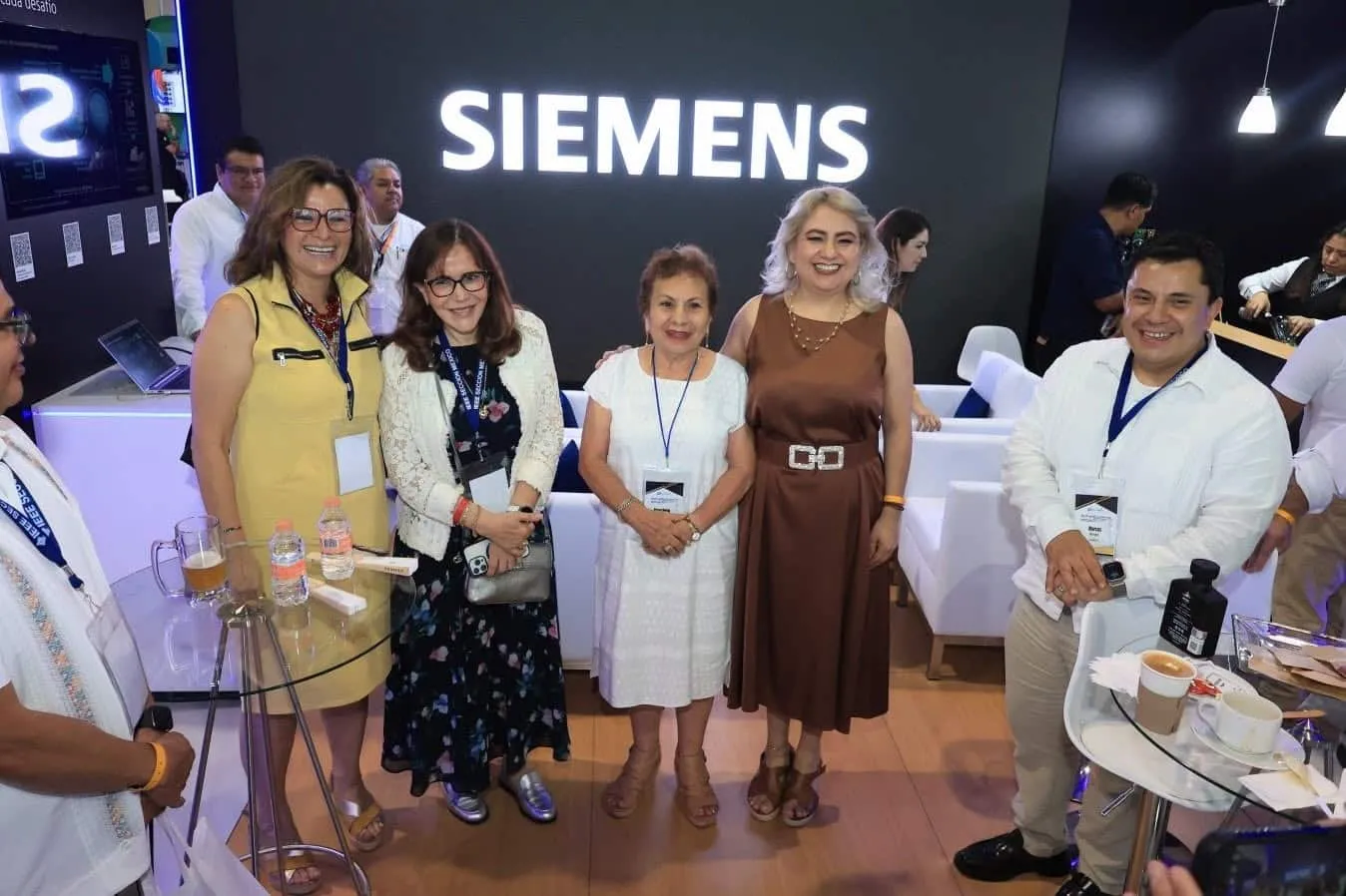 Group of six professionals posing for a photo in a Siemens booth at a conference or trade show, with a large SIEMENS sign in the background.