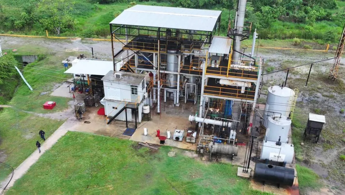 Aerial view of an industrial processing facility with a metal frame, pipes, and large cylindrical tanks surrounded by grass and gravel.