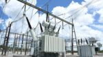 Outdoor electrical substation with a large transformer and high-voltage lines against a blue sky with clouds