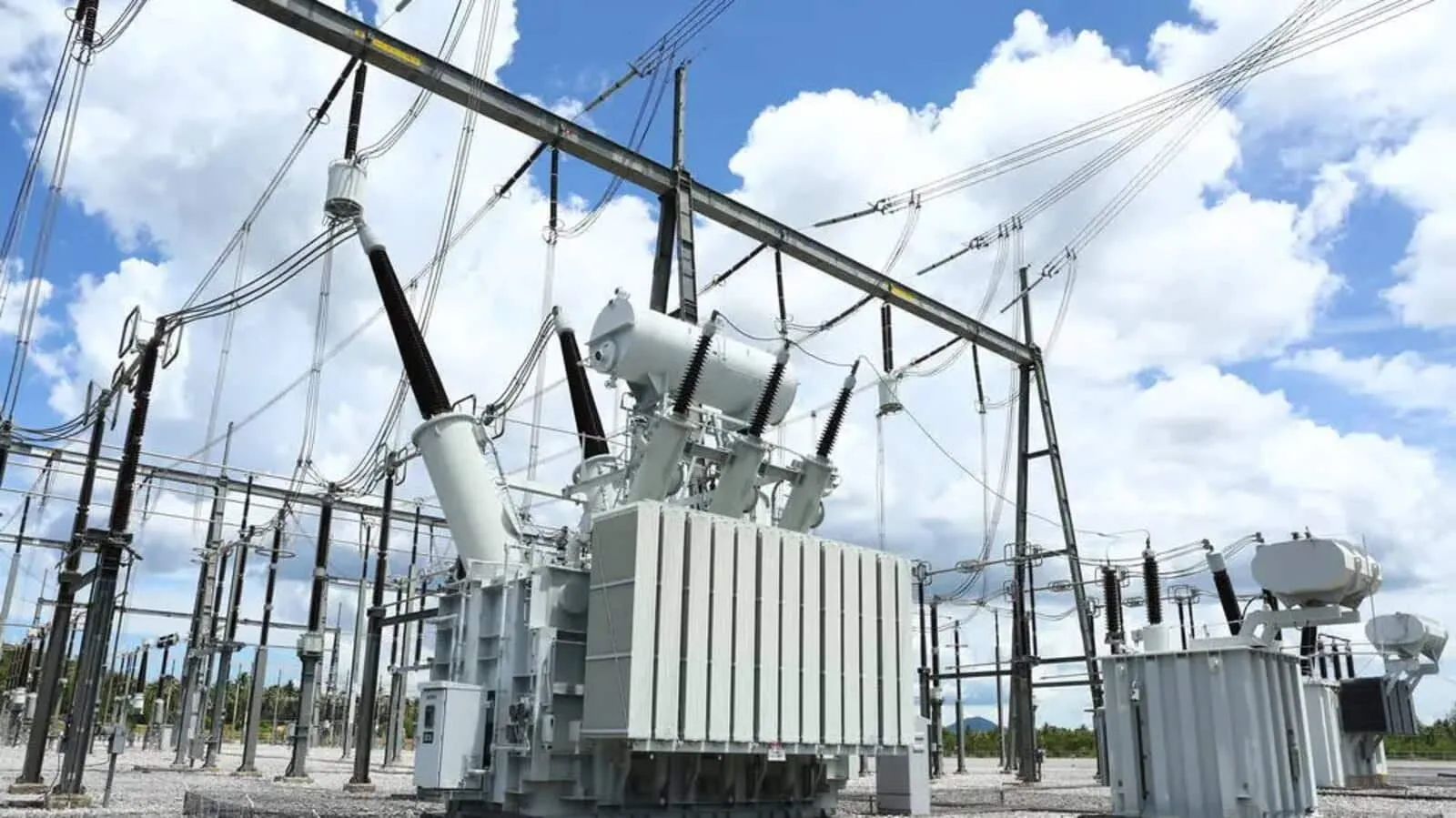 Outdoor electrical substation with a large transformer and high-voltage lines against a blue sky with clouds