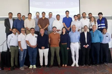 Group of professionals posing for a formal team photo on a stage at an indoor conference, with a projector screen behind them.