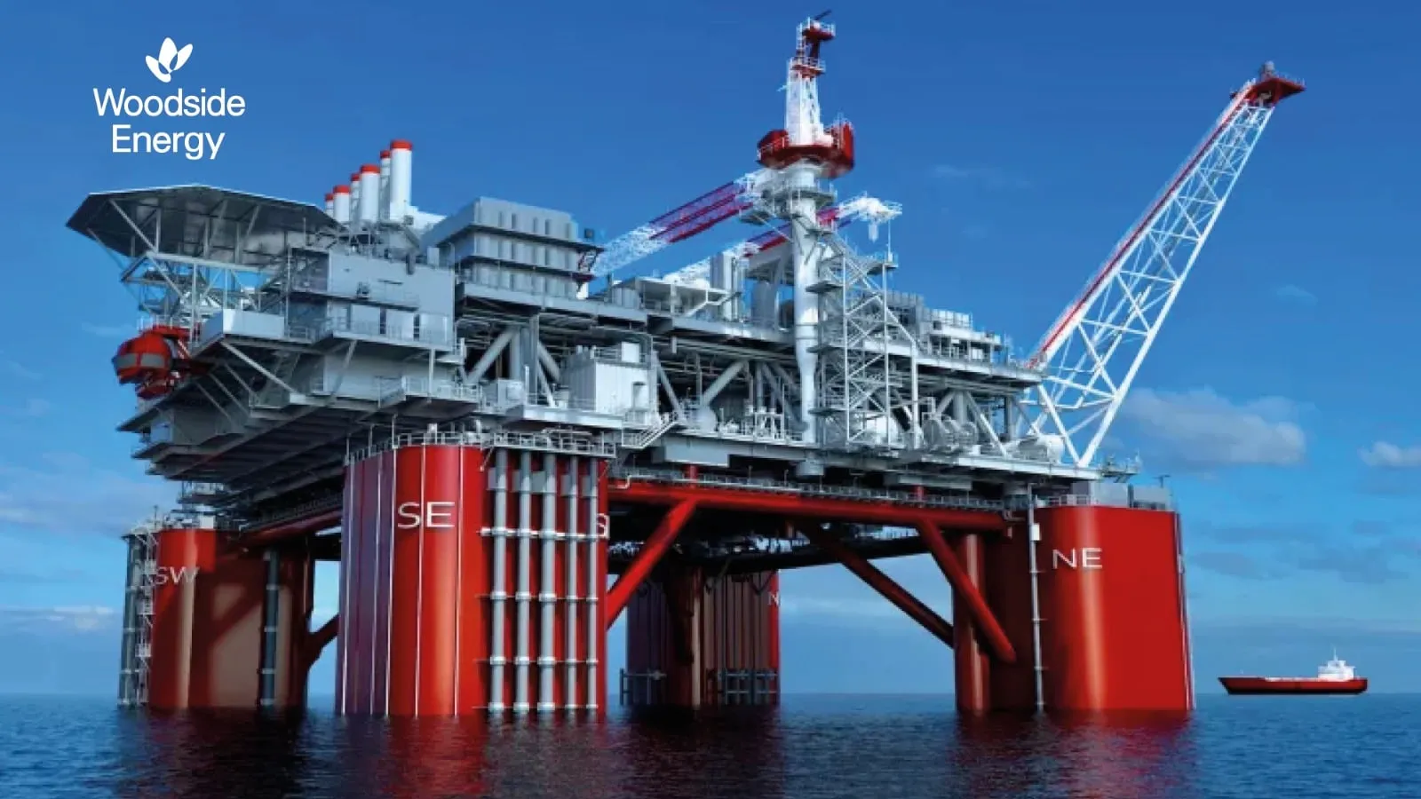 Offshore oil platform with red legs and a tall crane, Woodside Energy logo visible on the left against a blue sky and sea.