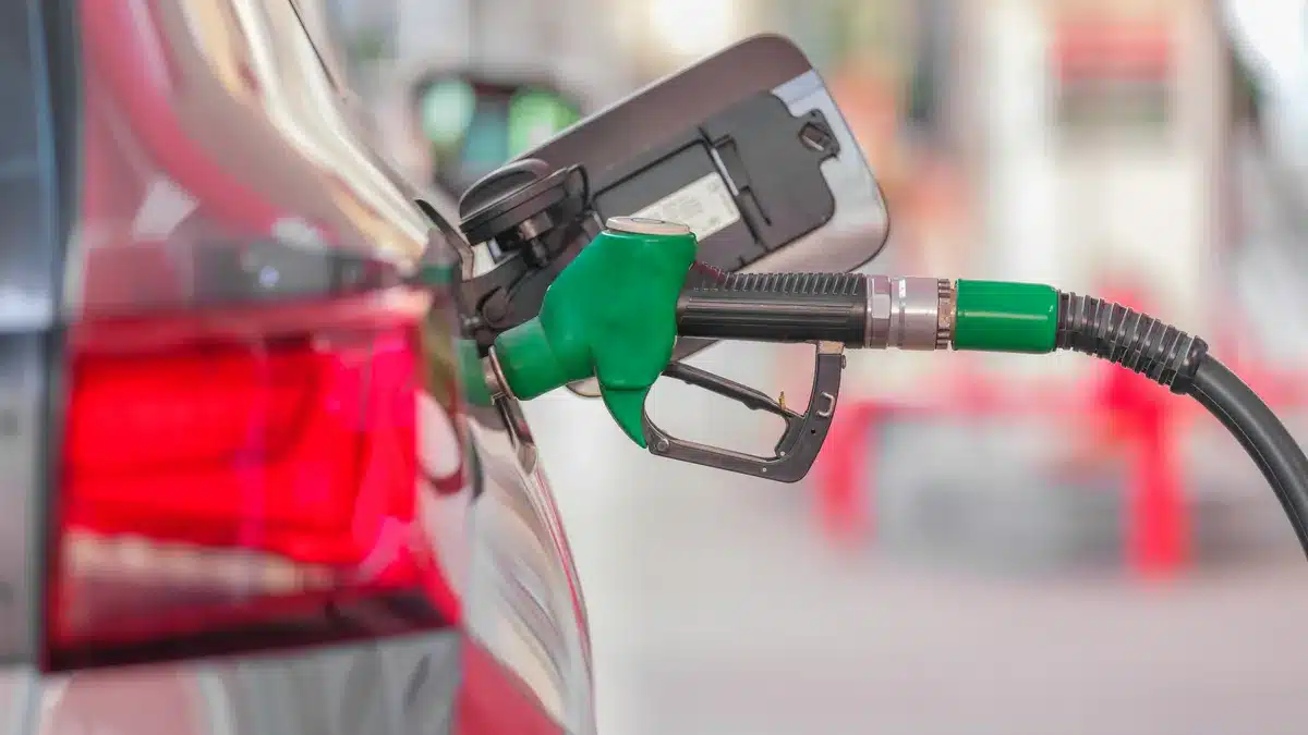 Green gasoline nozzle inserted into a car's fuel tank at a gas station