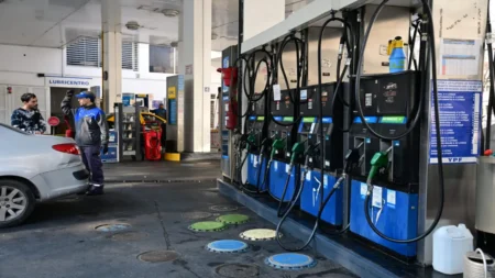 Gas station fuel pumps with hoses and a car being attended by a worker in a blue uniform at the pump area.