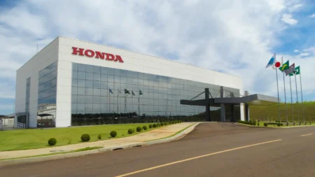Exterior view of a modern Honda building with a red HONDA sign, glass facade, and flagpoles along the driveway.