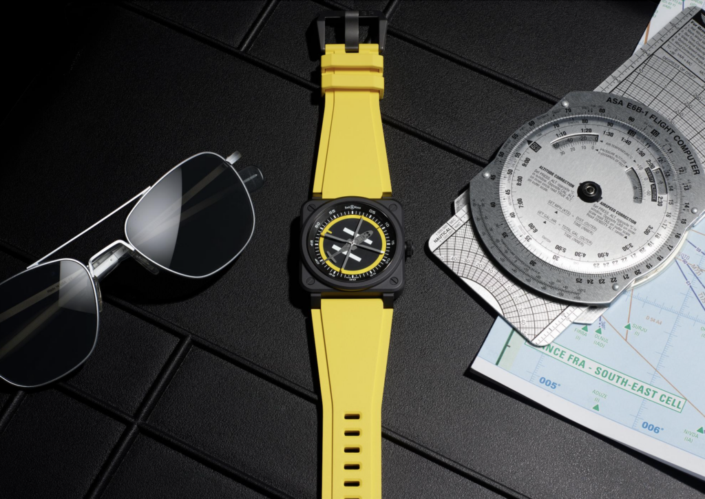 helipad 6 - Petróleo y Energía Close-up of a yellow wristwatch with a black dial on a dark textured surface, flanked by sunglasses and aviation charts on the right.