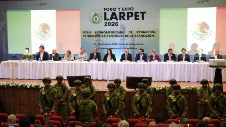 Panel of dignitaries sitting at a long table on a stage, with a banner reading 'FORO Y EXPO LARPET 2026' behind them; soldiers in camouflage march in front of the stage.