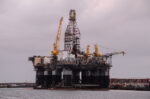Offshore oil rig platform with yellow cranes on calm sea, likely undergoing maintenance at sea edge.