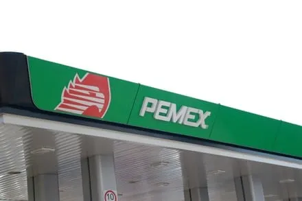 Green Pemex gas station canopy with the Pemex logo and emblem against a pale sky.
