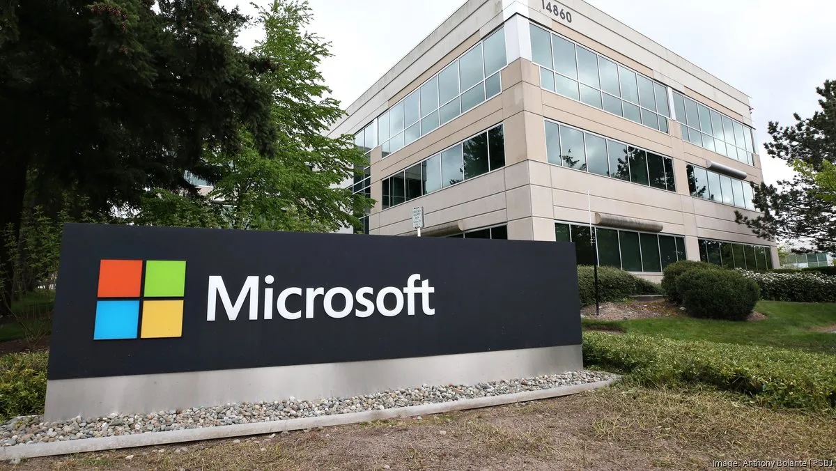 Microsoft sign on a black plaza sign with the colorful four-square logo in front of a beige office building with glass windows.
