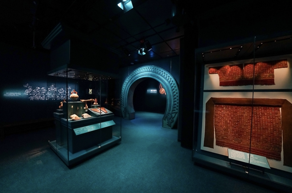 museo shangai 4 - Petróleo y Energía Dim museum gallery with a glass display case of artifacts and a blue decorative archway in the background.