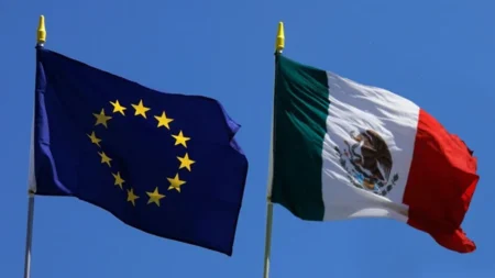 European Union flag beside the Mexican flag waving in the wind, against a clear blue sky