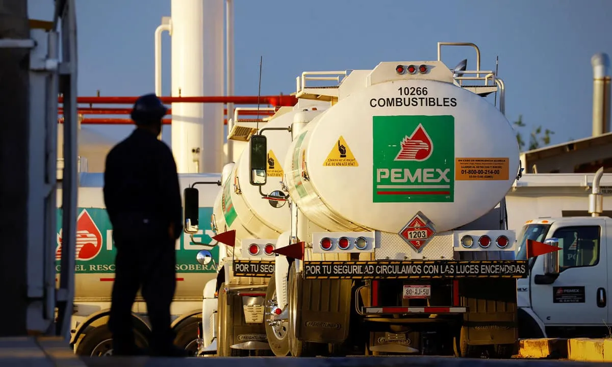 Fuel truck with PEMEX logo at a fueling terminal, a worker in dark clothing standing nearby silhouetted in the foreground