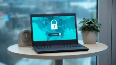 Laptop on a round table displaying a world map with a white padlock and a 'Secured' badge on the screen, with a plant nearby.