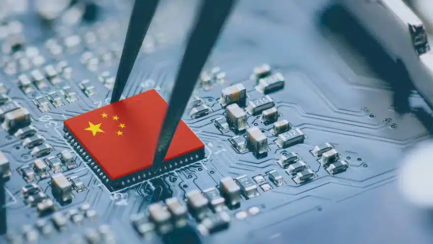 Close-up of a red microchip with the Chinese flag being placed on a circuit board by tweezers on a blue PCB backdrop.