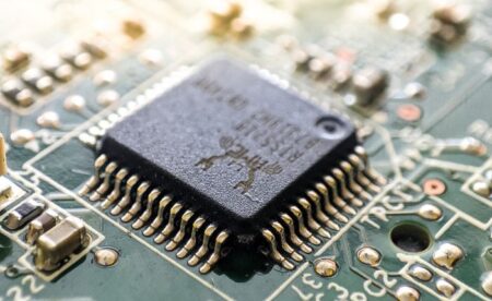 Close-up of a black integrated circuit with gold pins soldered to a green circuit board, viewed at an angle.