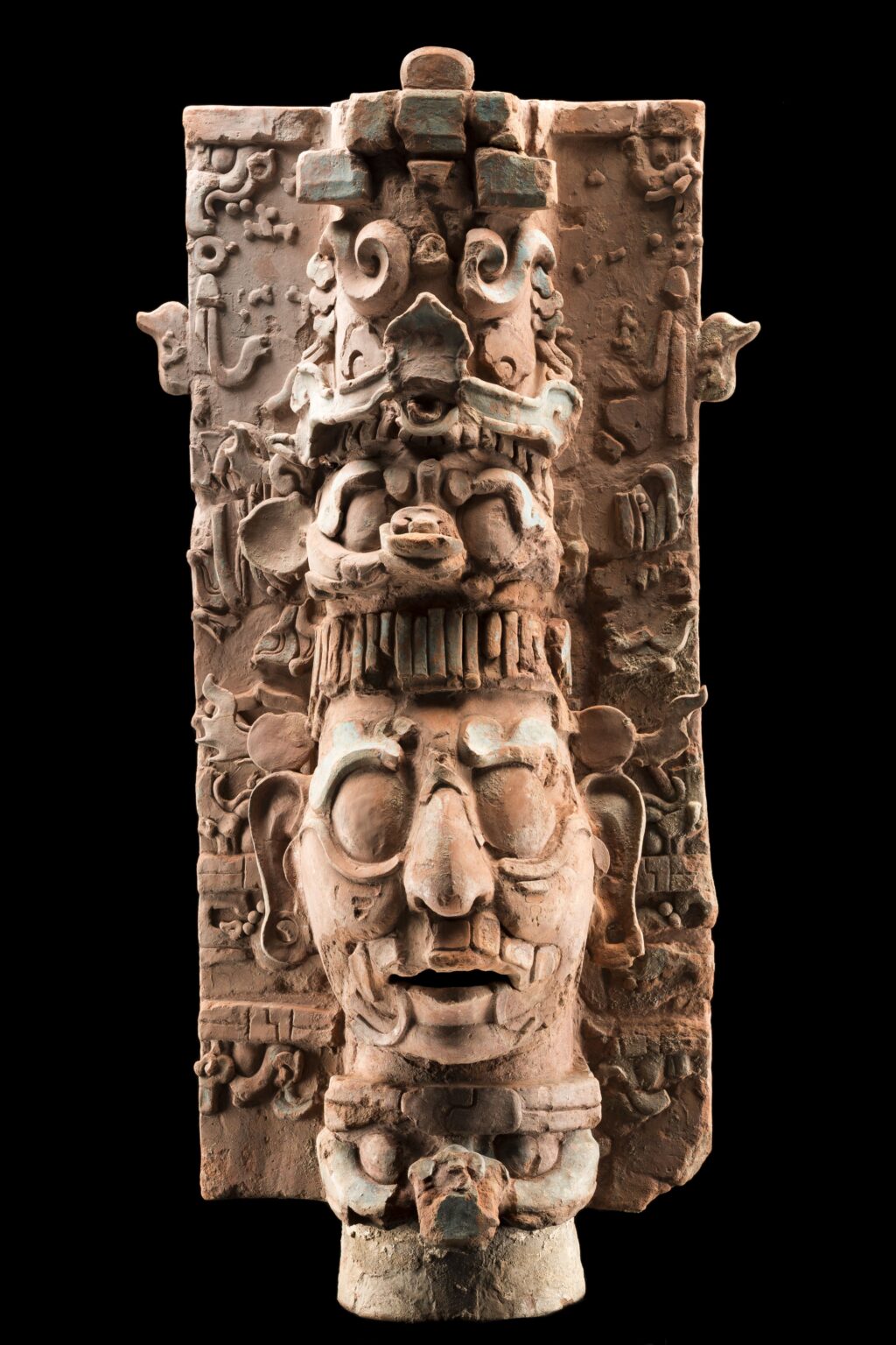 upload_202606_dc3bf0ee-fbe3-4100-9ada-8c2ae4a63aa0 - Petróleo y Energía Carved stone totem with a large, stylized face at the bottom and intricate mythic motifs along the shaft against a black background