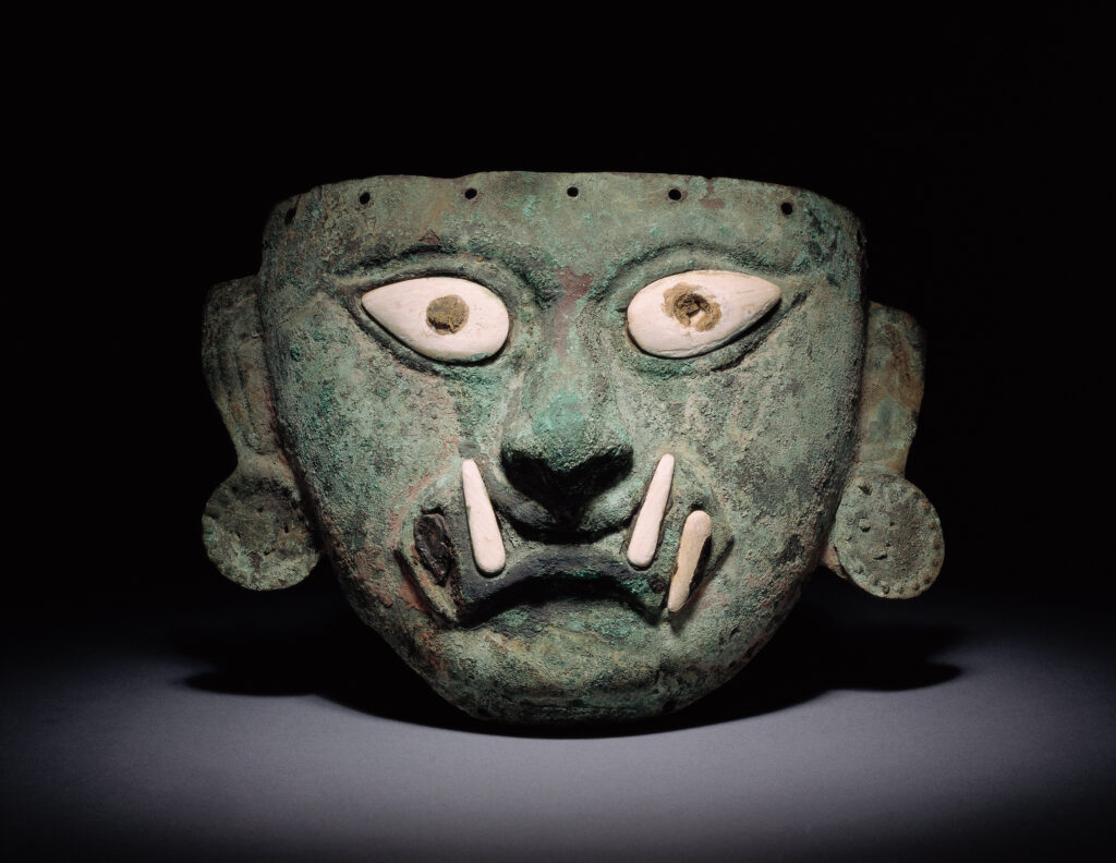 upload_202607_6e771601-adba-4852-9823-6d1515cb5f95 - Petróleo y Energía Close-up of a weathered green sculpture resembling a monster head with bulging white eyes and long white fangs against a dark background.
