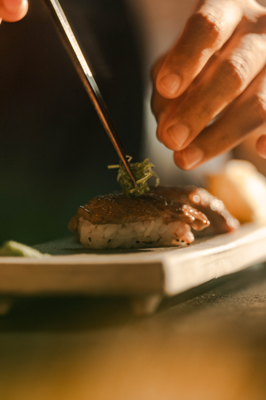 0I5A2787 - Petróleo y Energía Close-up of a chef using tweezers to garnish a piece of nigiri sushi with greens.