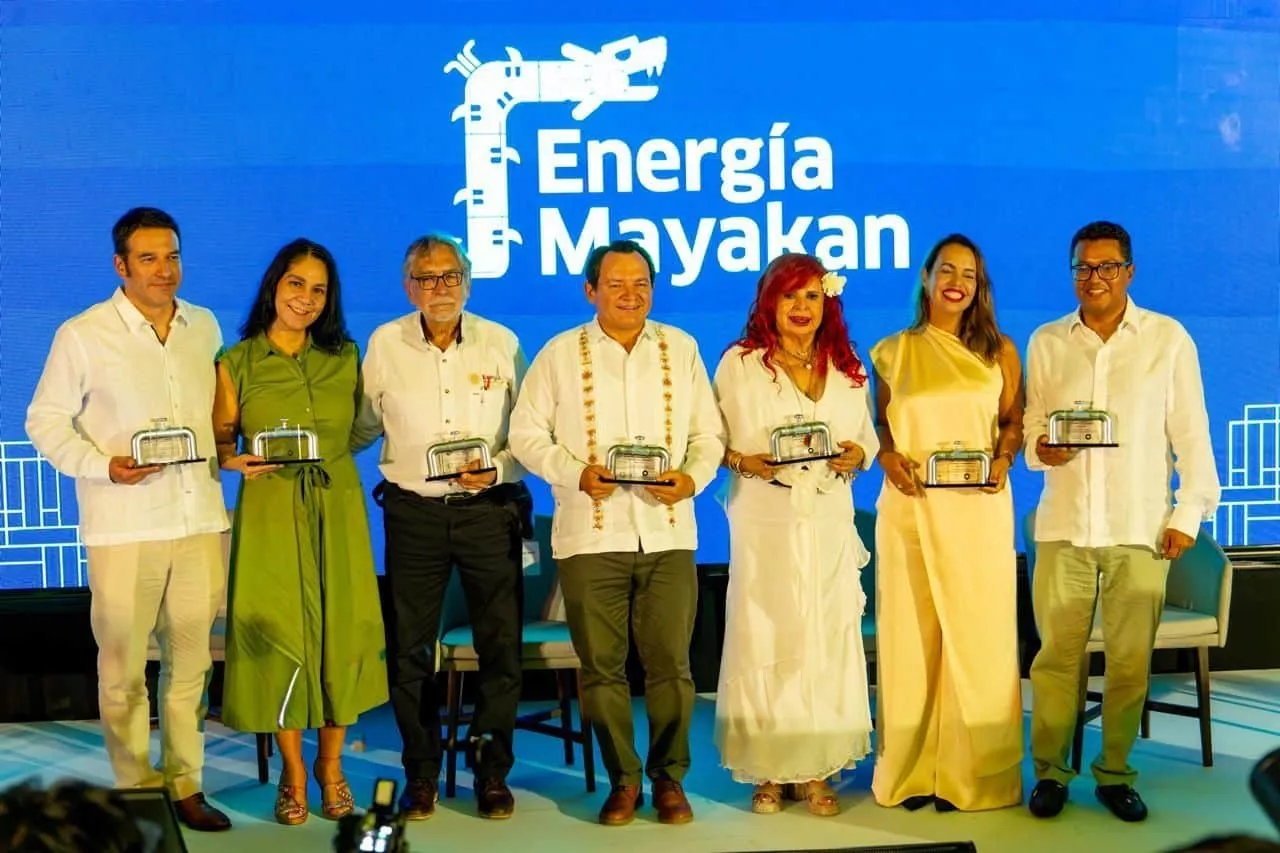 Seven people stand on a stage holding glass awards at an energy event; the blue backdrop reads 'Energía Mayakan'.