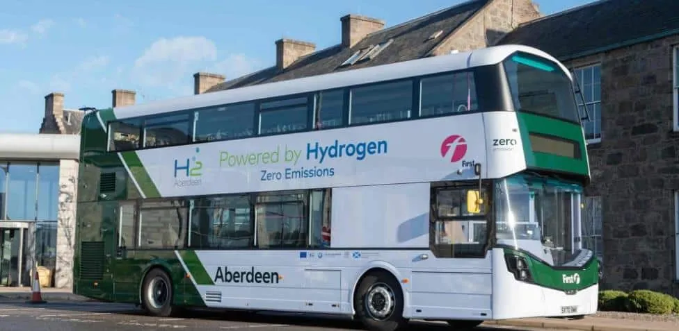 Hydrogen-powered double-decker bus with 'Powered by Hydrogen' branding parked outside a stone building in green and white livery.