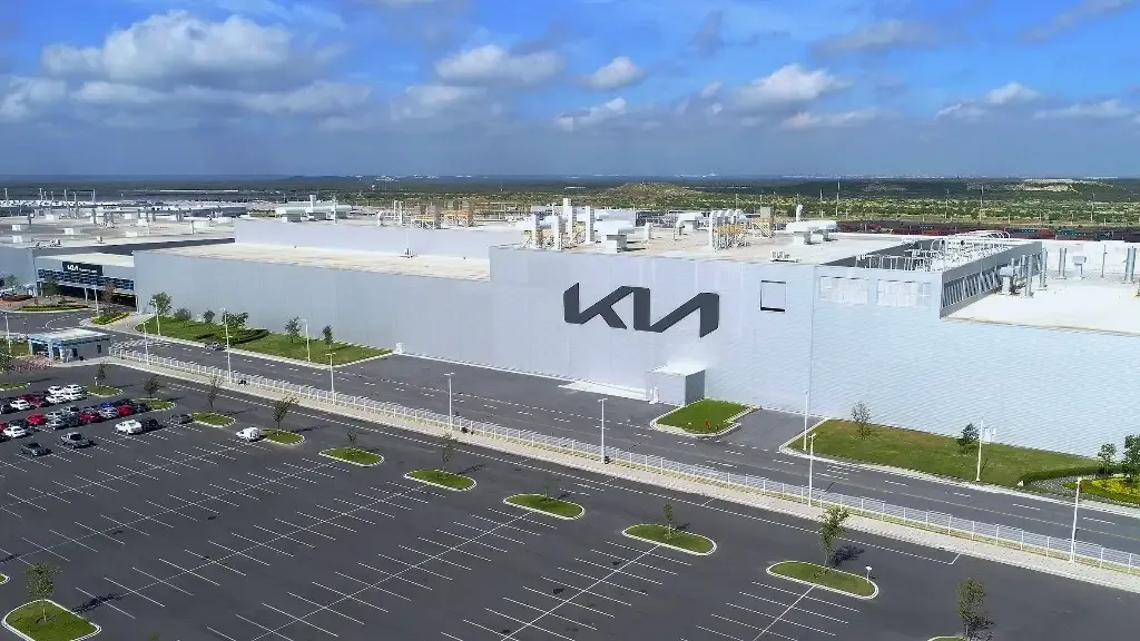 Aerial view of a large white Kia building with an expansive parking lot and a blue sky above.