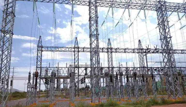 High-voltage electrical substation with metal lattice towers, insulators, and wiring under a blue sky.
