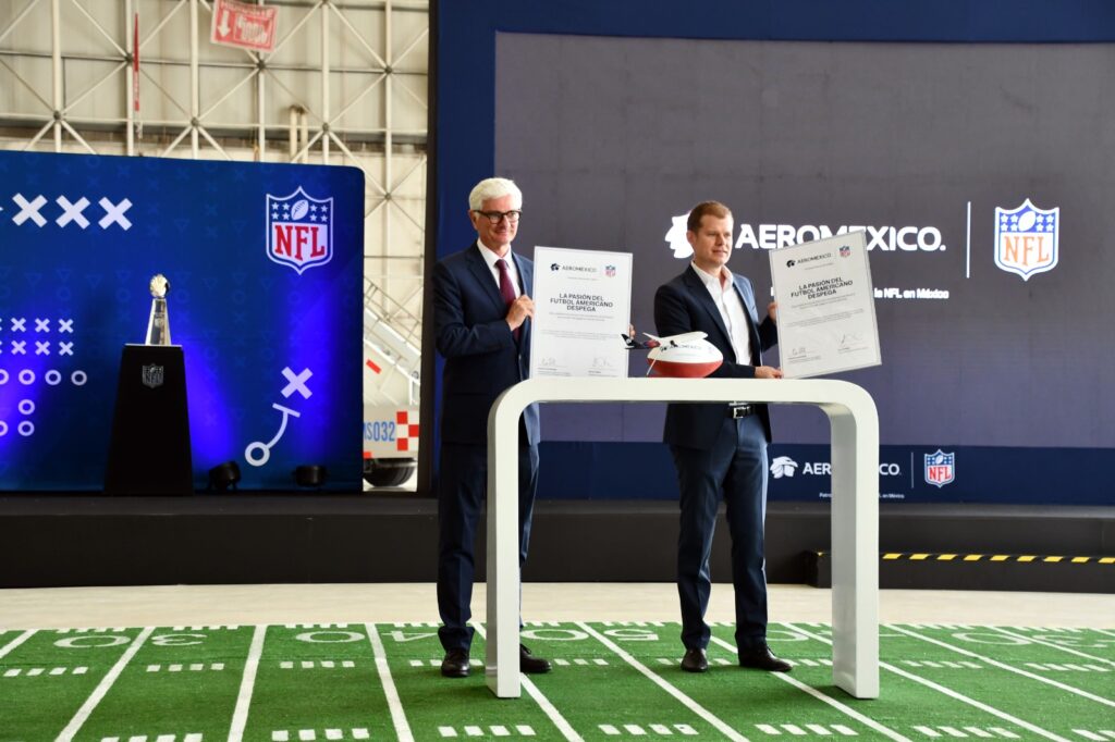 AEROMEXICO 3 - Petróleo y Energía Two suited men hold large certificates on a stage with an NFL/Aeromexico backdrop and a football on a white table nearby
