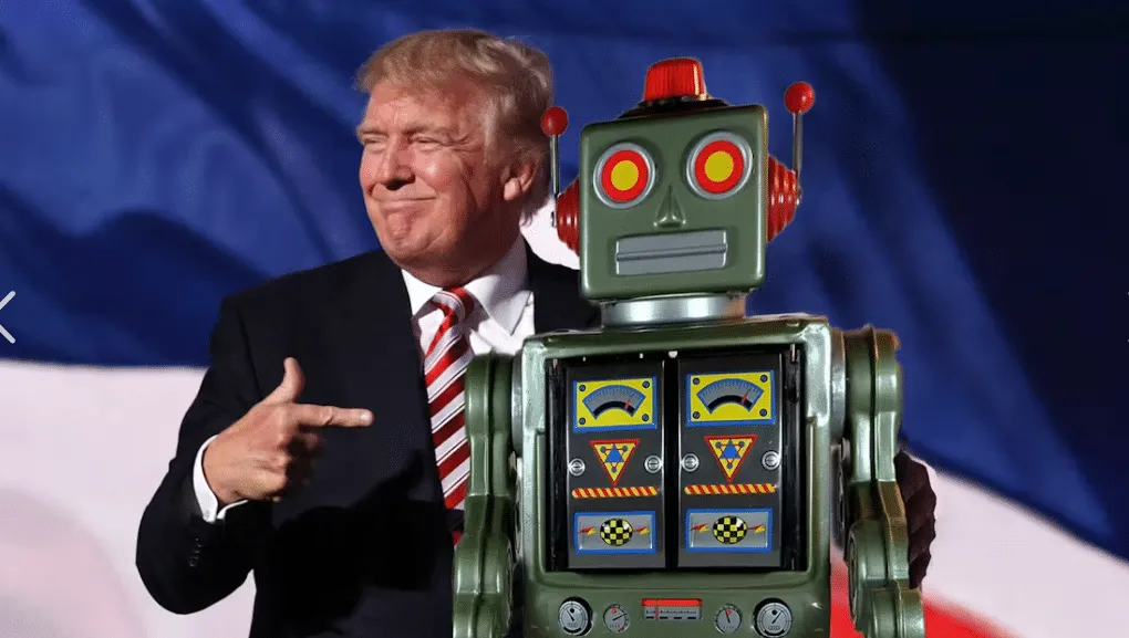 Man in a dark suit smiles and points at a vintage green tin robot on a stage against a blue backdrop.