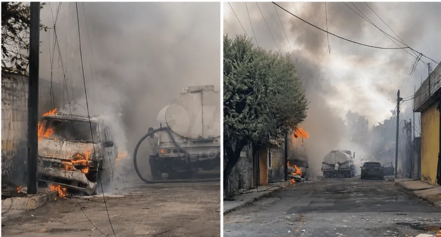 Two vehicles on a smoky street are on fire, with flames and thick smoke rising near utility poles and a tanker truck behind.
