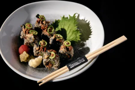 Sushi rolls topped with jalapeño slices and sesame seeds on a white plate with a green leaf and chopsticks nearby