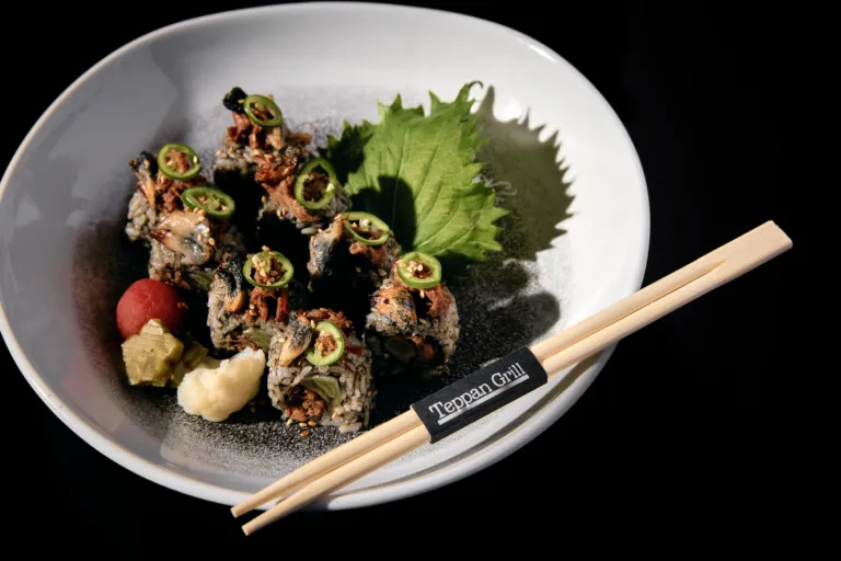 Sushi rolls topped with jalapeño slices and sesame seeds on a white plate with a green leaf and chopsticks nearby